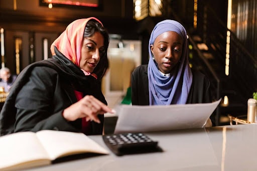 Two women in hijabs review financial documents and calculations, illustrating Islamic finance services in Australia.